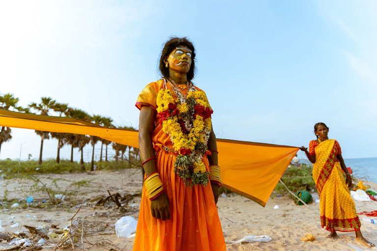 A devotee dressed in vibrant orange stands by the beach during Kulasai Dasara